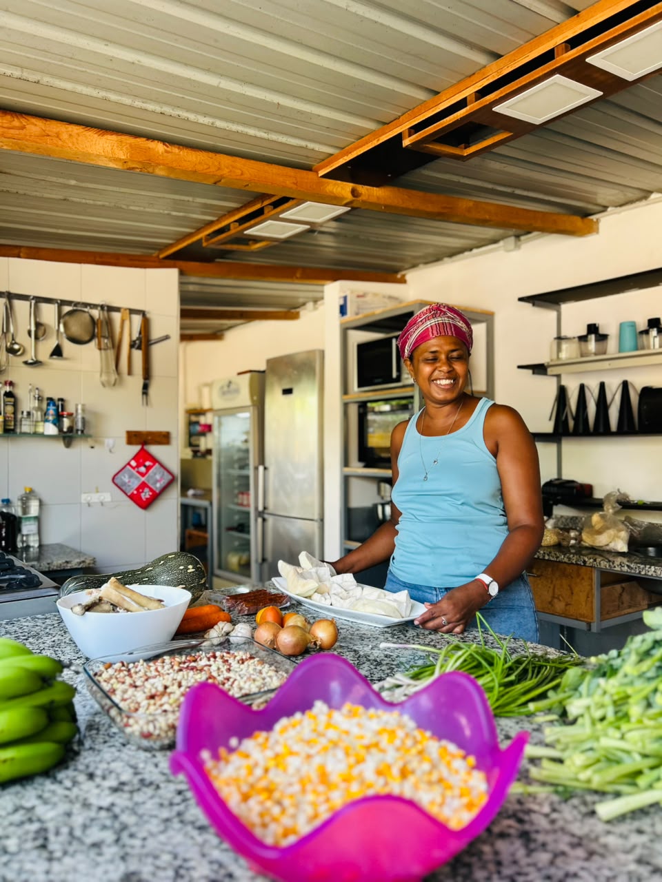 Aldina na cozinha, com milho, feijão e legumes frescos